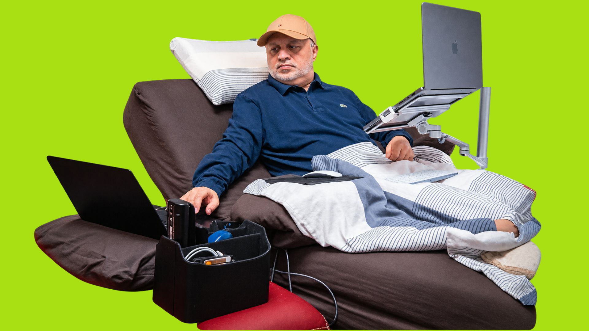 Nadeem Arif working from his bed, a laptop mounted on a stand in front of him