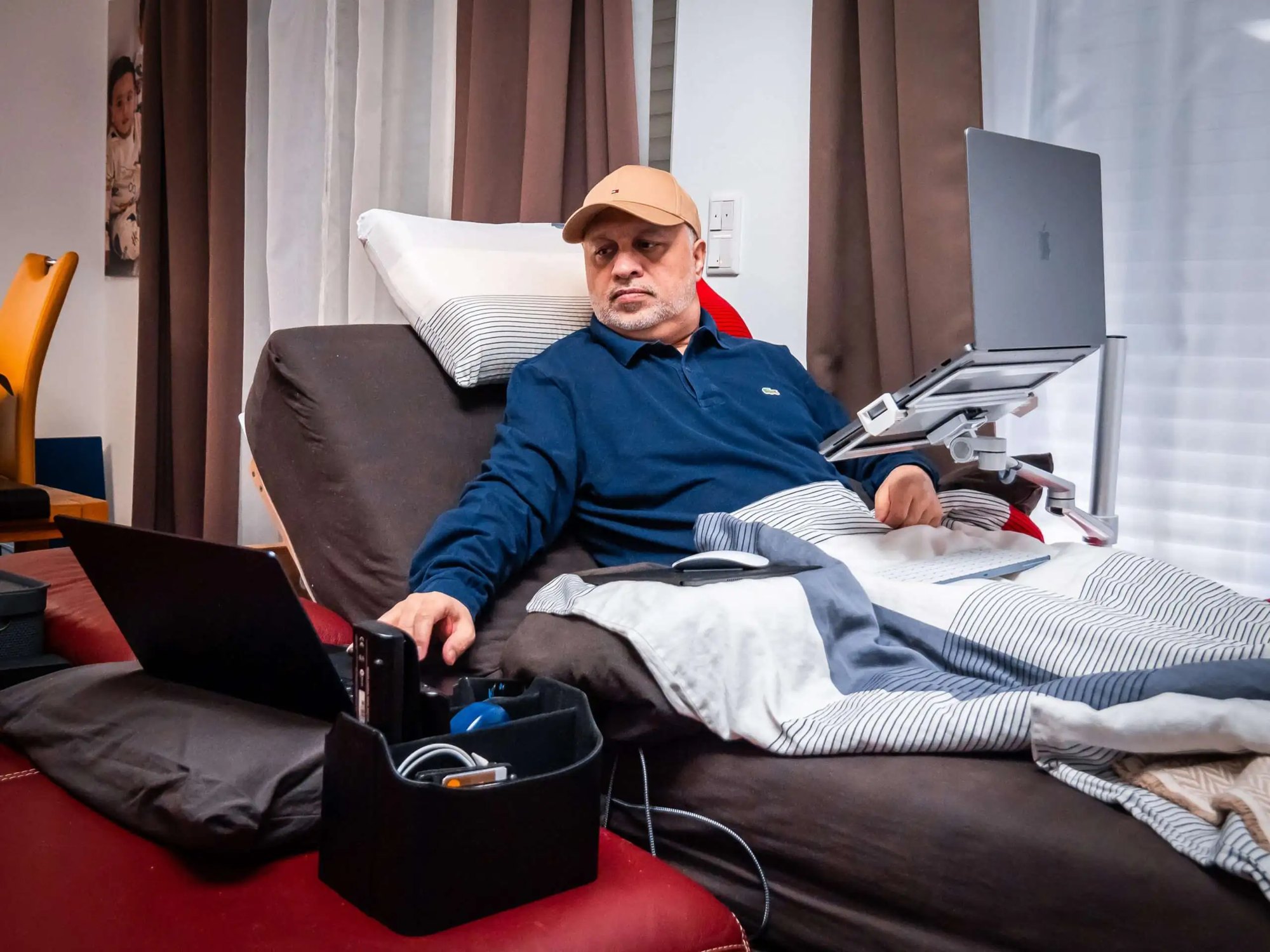 Nadeem Arif working from his bed, a laptop mounted on a stand in front of him